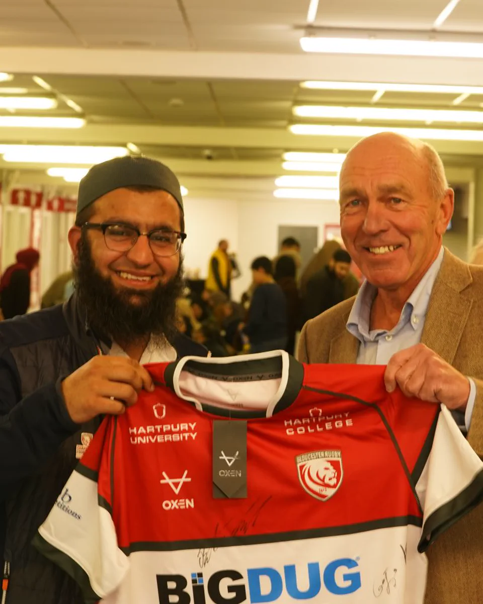 Two men holding a signed Gloucester Rugby shirt at a community event